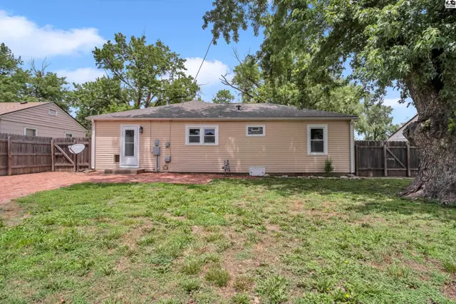 Backyard view of a single-story home with tan siding, a white door, and a fenced yard.