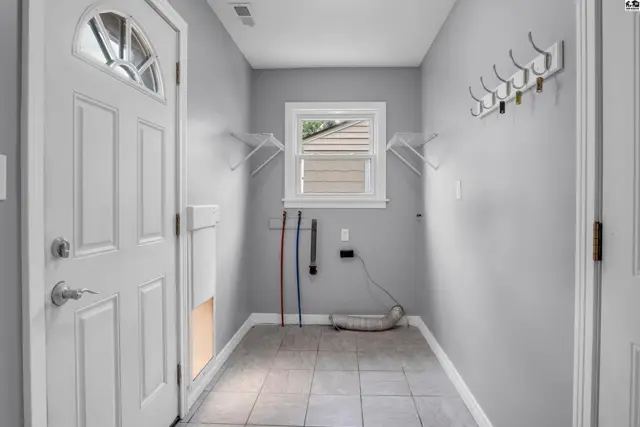 Laundry room with tiled floor, white door, and utility hookups.