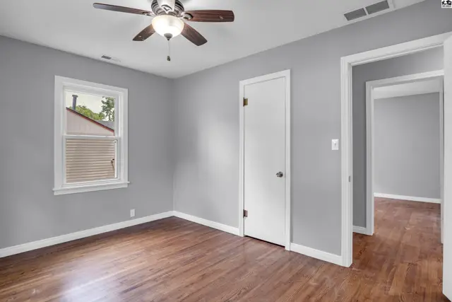 Bedroom with gray walls, hardwood floors, ceiling fan, and a doorway to another room.