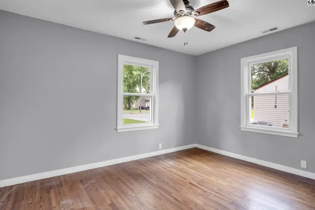 Bright bedroom with gray walls, hardwood floors, and two windows offering natural light.