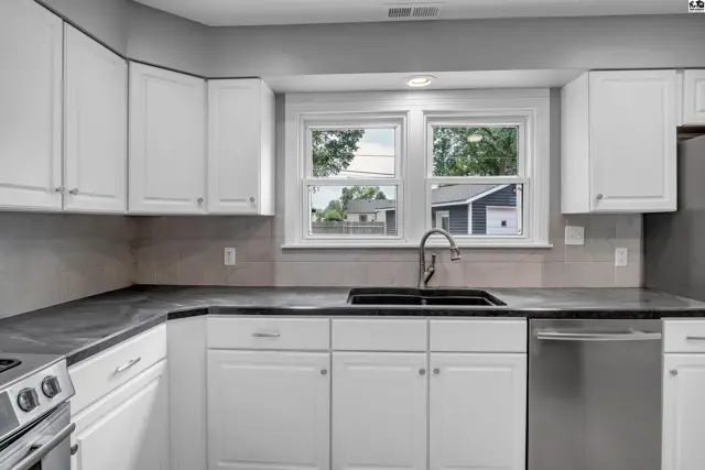 Modern kitchen with white cabinets, gray tiled backsplash, dark countertops, and stainless steel appliances.