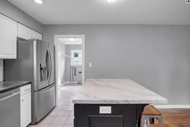 Modern kitchen with stainless steel appliances, marble island, and light gray walls.