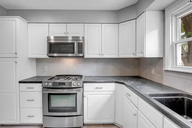 Modern kitchen with white cabinets, stainless steel appliances, and dark countertops.