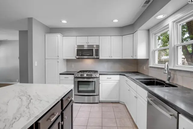 Modern kitchen with white cabinets, stainless steel appliances, dark countertops, and a marble island.