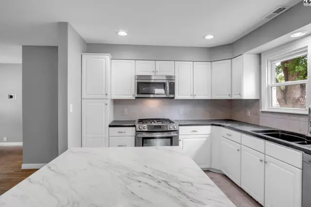 Modern white kitchen with marble island, stainless steel appliances, and dark countertops.