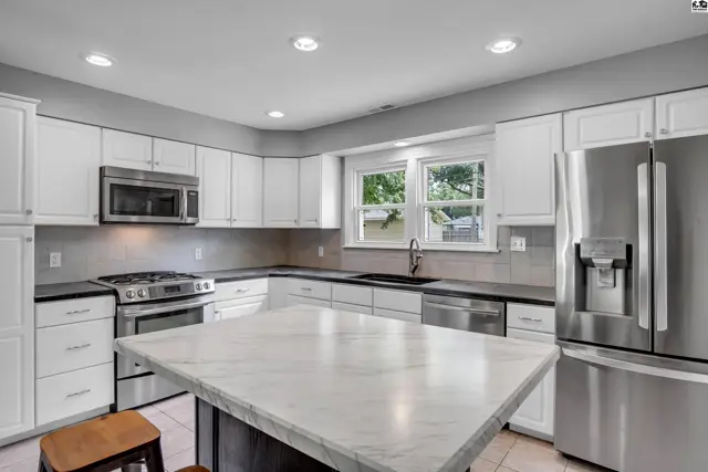 Modern white kitchen with marble island, stainless steel appliances, and granite countertops.