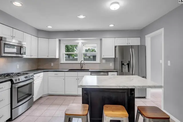 Modern kitchen with white cabinets, stainless steel appliances, and a dark island with a marble countertop.