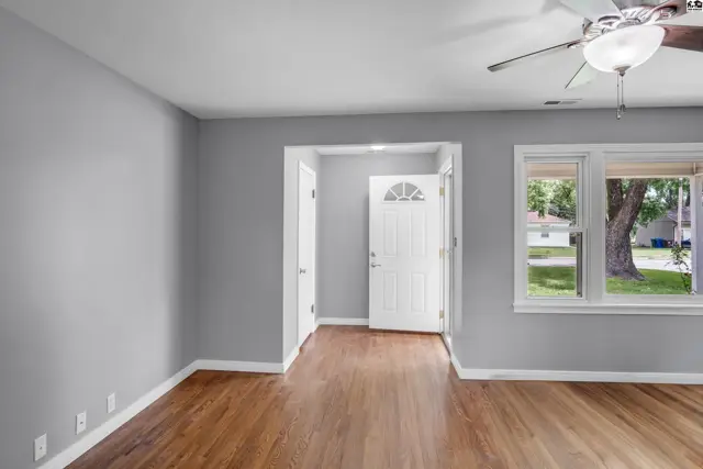 Bright living room with gray walls, wood-look flooring, and a view of the front door and exterior.