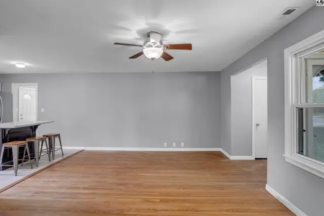 Spacious living area with hardwood floors, gray walls, and a modern ceiling fan.