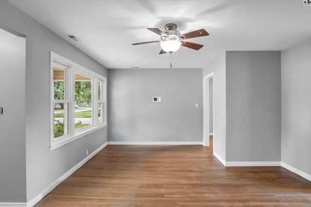 Spacious living room with hardwood floors, large windows, and a ceiling fan.