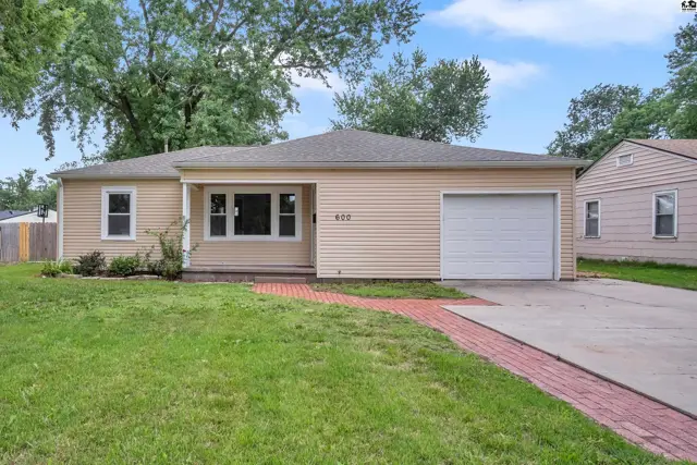Exterior of a light yellow, single-story home with beige siding, a white garage door, and a brick walkway.