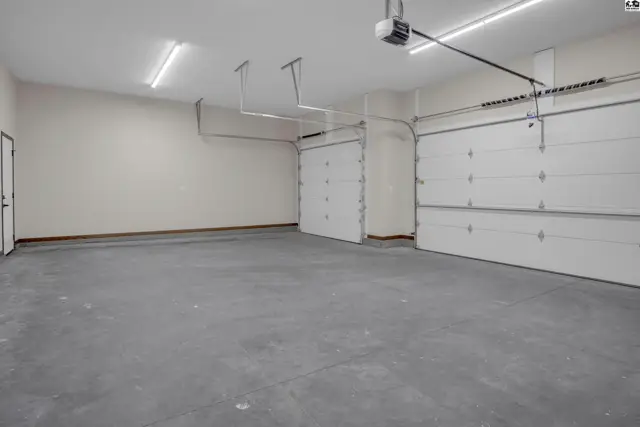 Spacious garage with concrete floor, white walls, and three overhead doors.