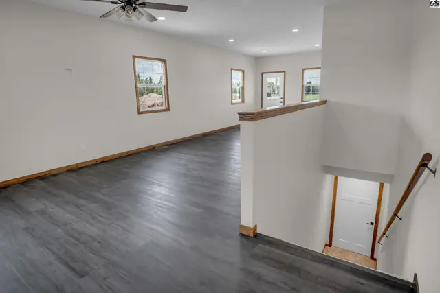 Spacious living area with dark wood-look flooring, white walls, and natural light from multiple windows.