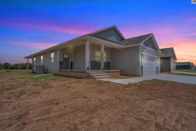 Modern gray home with stone accents, a covered porch, and a two-car garage under a colorful twilight sky.