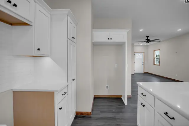 Modern white kitchen cabinets and countertops with dark wood flooring leading to a living area.