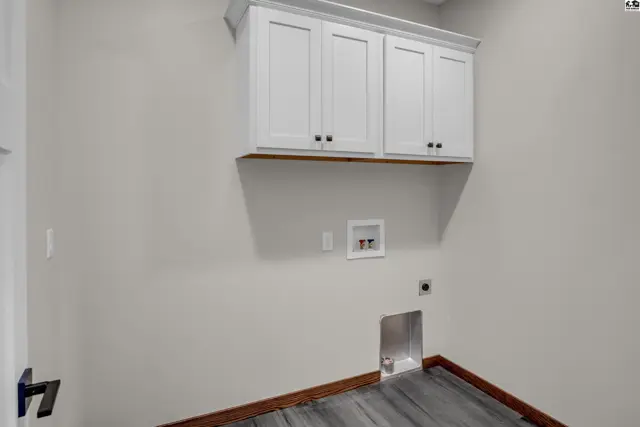 Laundry room with white cabinets, gray wood-look flooring, and dark wood trim.
