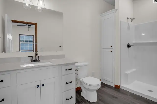 Modern white vanity with quartz countertop, dark wood-look flooring, and a walk-in shower.