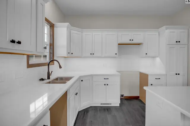 Modern white kitchen with quartz countertops, stainless steel sink, and dark wood floors.