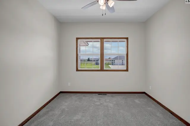 Empty room with gray carpet, neutral walls, wood trim, and a ceiling fan.