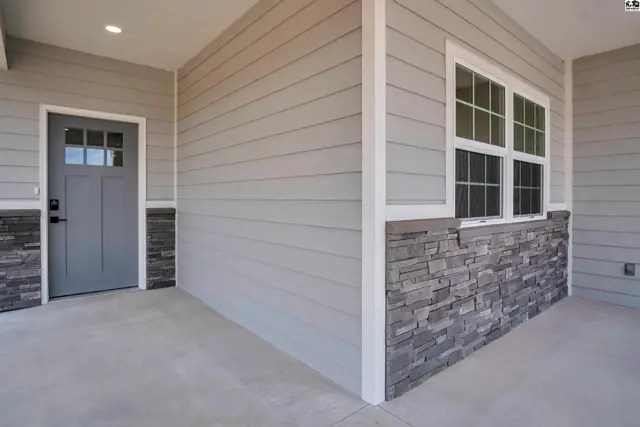 Exterior entryway with gray siding, stone accents, and a glass-paneled door.