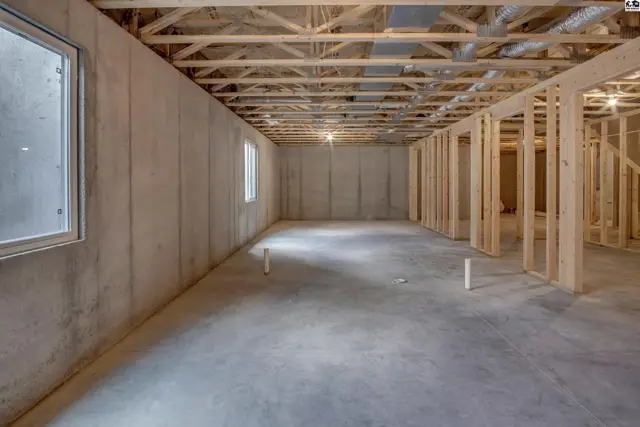 Unfinished basement with concrete walls and floor, exposed wood framing, and small windows.