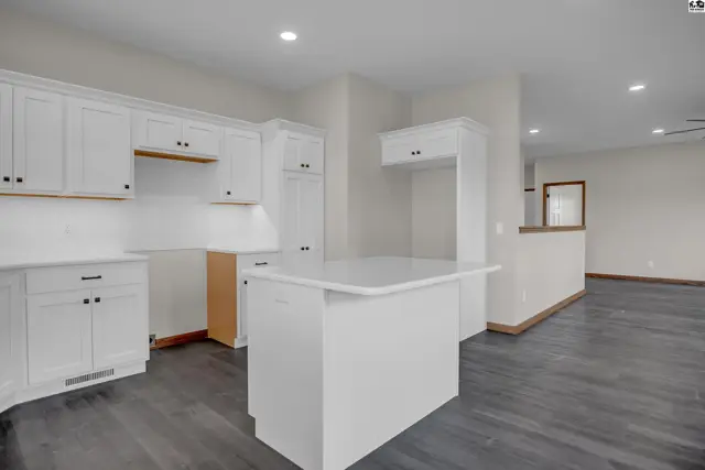 Modern white kitchen with a central island, dark wood-look flooring, and ample cabinet space.