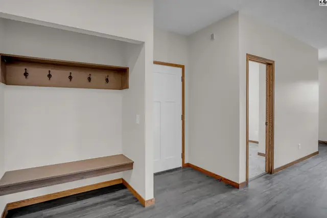 Entryway with built-in bench, coat hooks, white door, and dark wood trim.
