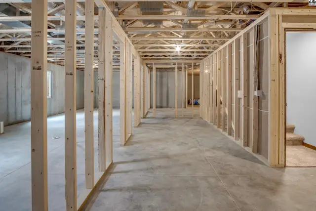 Unfinished basement with concrete floors, exposed joists, and wood framing for new rooms.