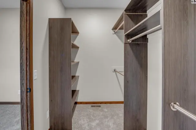 Spacious walk-in closet with dark wood shelving, hanging rods, and neutral carpet.