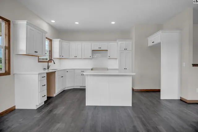 Spacious white kitchen with a central island, dark wood-look flooring, and stainless steel appliances.