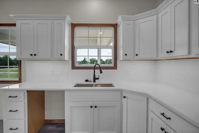 Modern white kitchen with quartz countertops, stainless steel sink, and dark hardware.