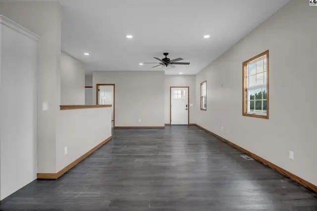 Spacious living room with dark wood-look flooring, white walls, and a ceiling fan.