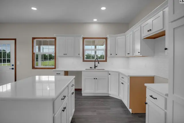Spacious white kitchen with quartz countertops, dark wood floors, and ample cabinet space.