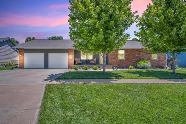 Brick ranch home with a two-car garage, manicured lawn, and inviting front porch.