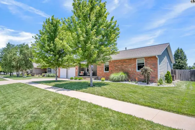 Brick and siding ranch home with a manicured lawn and mature trees.
