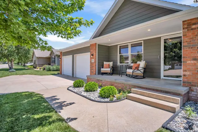Modern home exterior with gray siding, brick accents, a covered porch with seating, and a three-car garage.