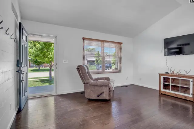 Living room with vaulted ceiling, dark wood floors, recliner, and TV on a rustic media console.