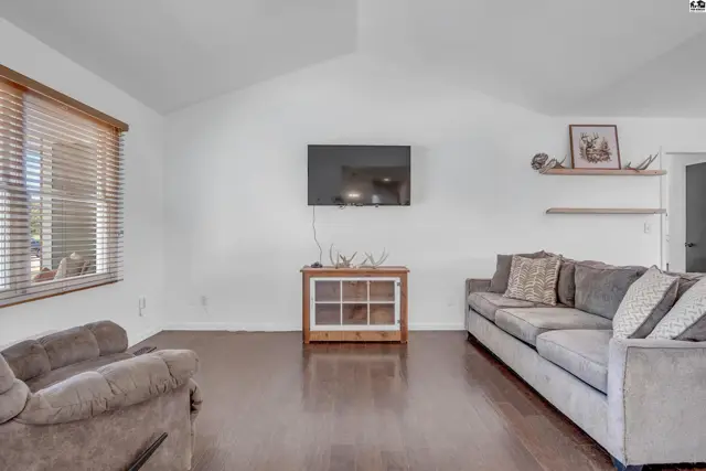 Living room with vaulted ceiling, dark wood floors, gray sofas, and a mounted television.