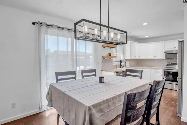 Dining area with a table, chairs, and modern chandelier, adjacent to a white kitchen.