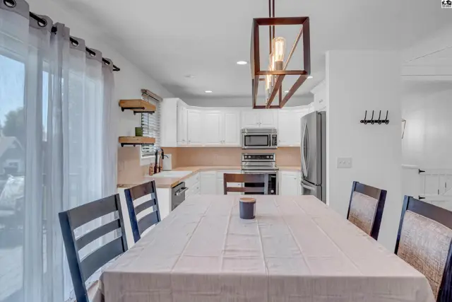 Modern kitchen with white cabinets, stainless steel appliances, and a dining table set for a meal.