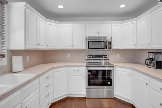 Spacious white kitchen with stainless steel appliances, light countertops, and dark wood floors.