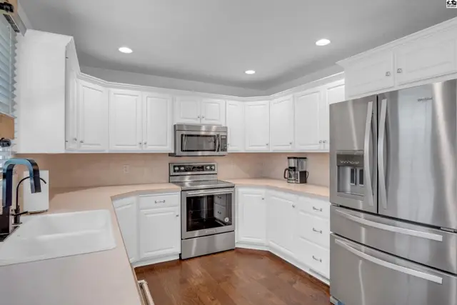 Bright white kitchen with stainless steel appliances, granite countertops, and dark wood floors.