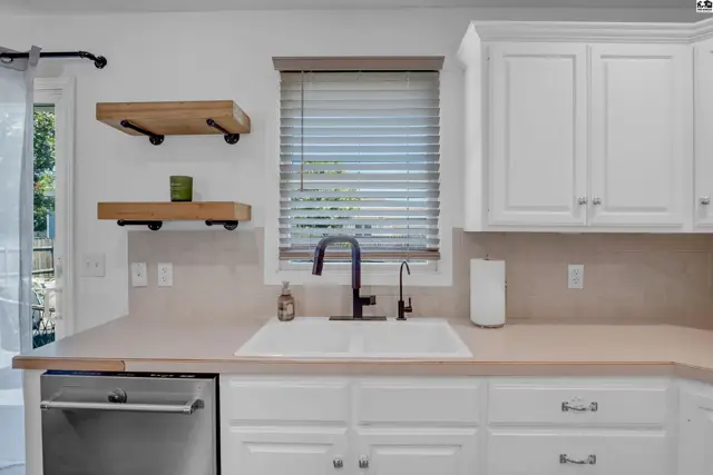 Bright kitchen with white cabinets, double sink, butcher block counters, and open shelving.
