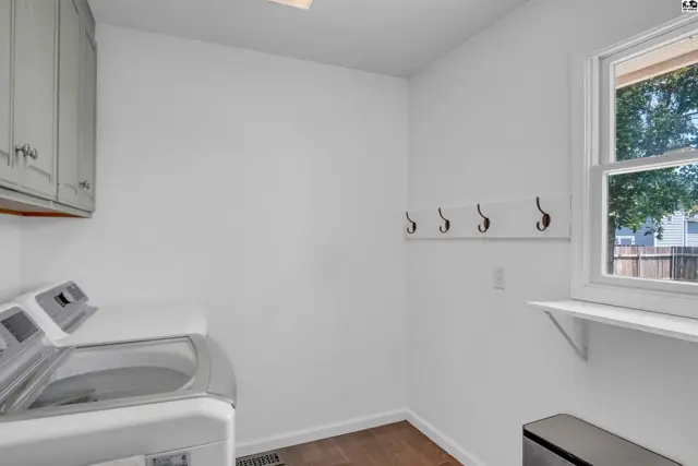 Bright laundry room with a modern washer, gray cabinets, and a white coat rack.