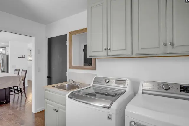 Modern laundry room with white appliances, light gray cabinets, and a stainless steel sink.