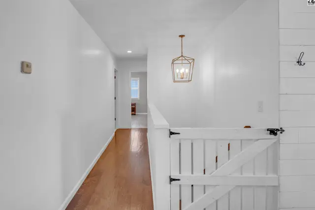 Bright hallway with white walls, hardwood floors, and a modern geometric pendant light.