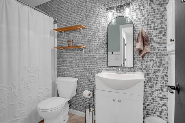 Modern bathroom with a white vanity, arched mirror, and textured gray wallpaper.