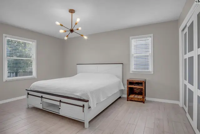 Spacious bedroom with a white bed, wood accents, and modern light fixture.