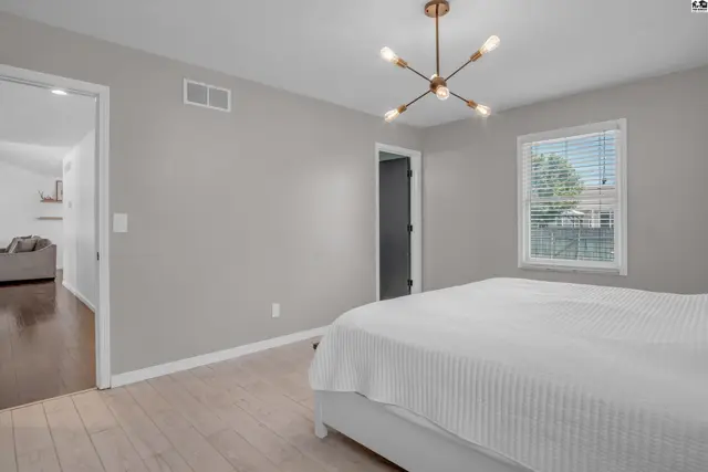Modern bedroom with light wood floors, gray walls, and a stylish Sputnik chandelier.