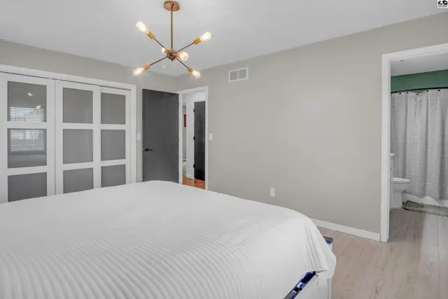 Spacious bedroom with a modern sputnik chandelier, white paneled closet doors, and light wood flooring.